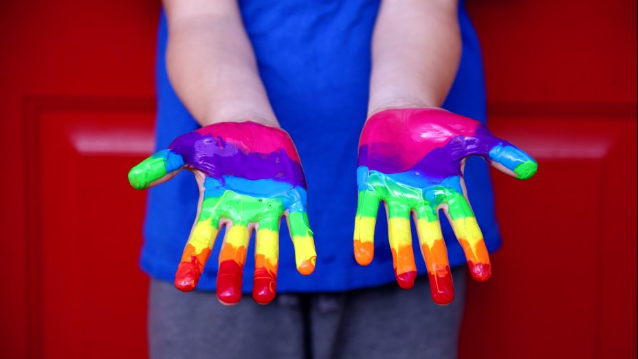 Kind mit bemalten Handinnenflächen in Regenbogenfarben