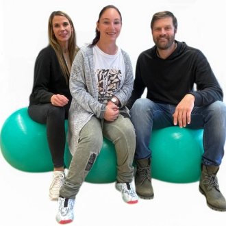 Bianca, Tanja und Alois sitzen l&auml;chelnd nebeneinander auf gro&szlig;en, t&uuml;rkisfarbenen Gymnastikb&auml;llen vor einem neutralen, wei&szlig;en Hintergrund. 