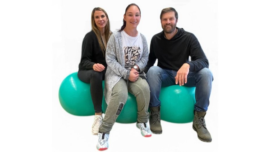 Bianca, Tanja und Alois sitzen l&auml;chelnd nebeneinander auf gro&szlig;en, t&uuml;rkisfarbenen Gymnastikb&auml;llen vor einem neutralen, wei&szlig;en Hintergrund. 